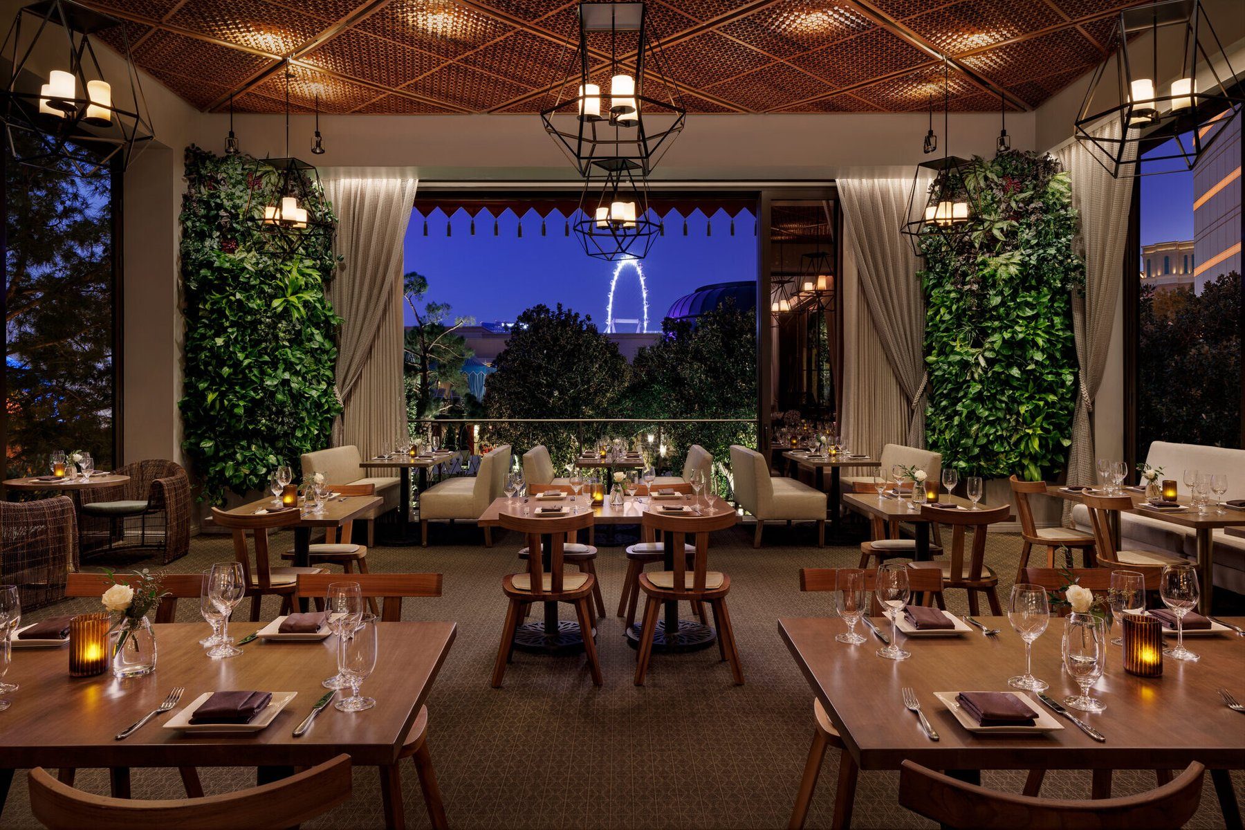 The Garden Room at La Cave Wine & Food Hideaway inside Wynn Las Vegas at blue hour — living walls, lantern chandeliers, and the High Roller lit in the window.